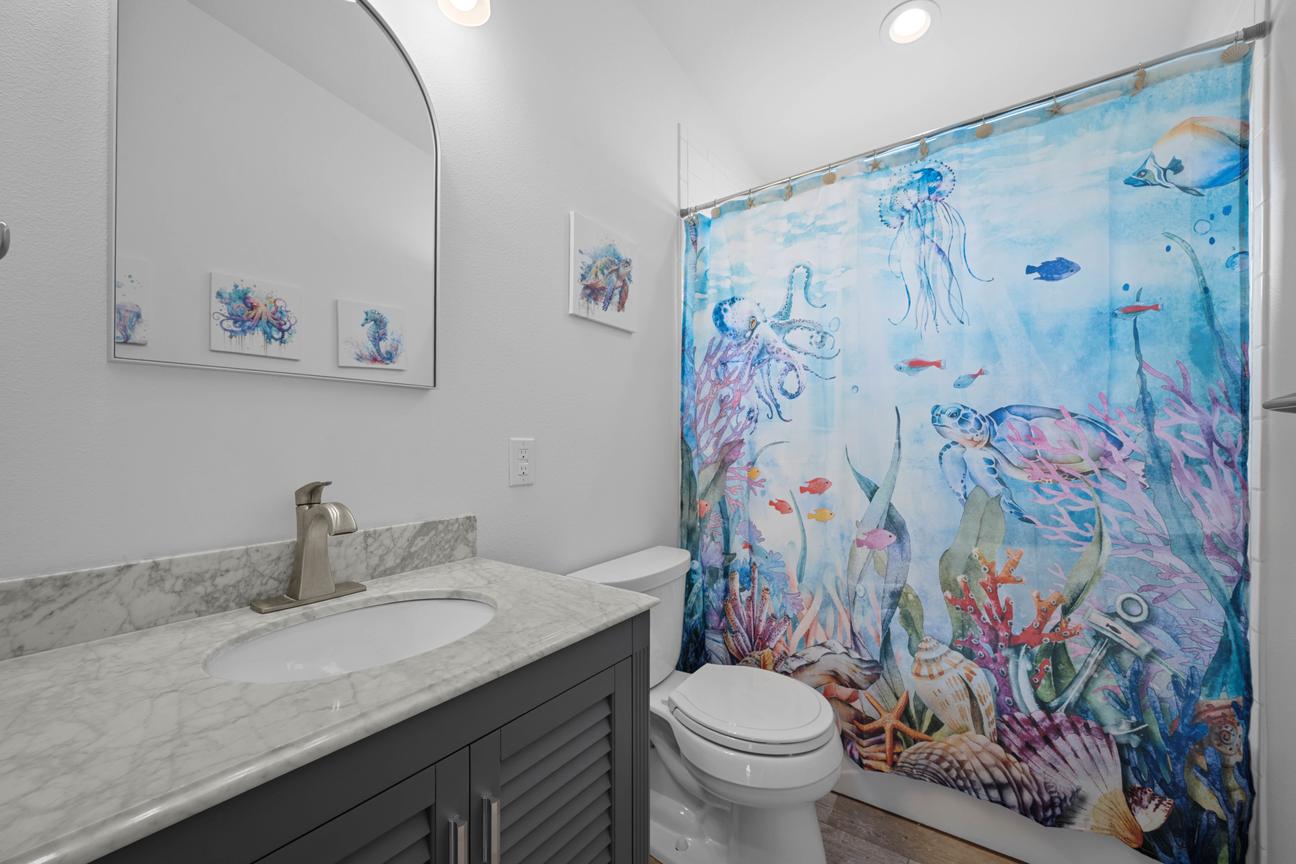 Shared bathroom with a gray vanity, tub-and-shower combination, and a colorful marine-life shower curtain.