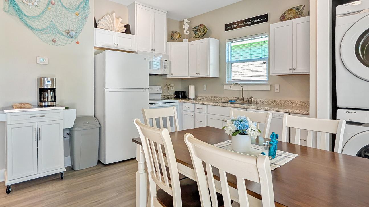 Bright open kitchen with dining table that seats six, while appliances and white cupboards, window above sink.