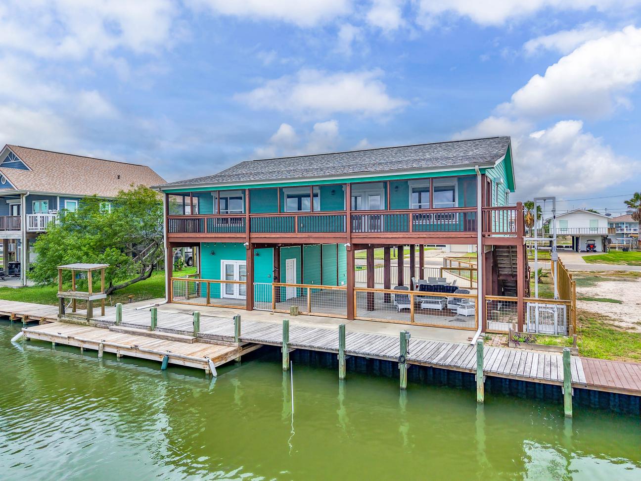 Colorful two-story canal-front vacation home with covered decks, outdoor seating, and a private wooden dock.