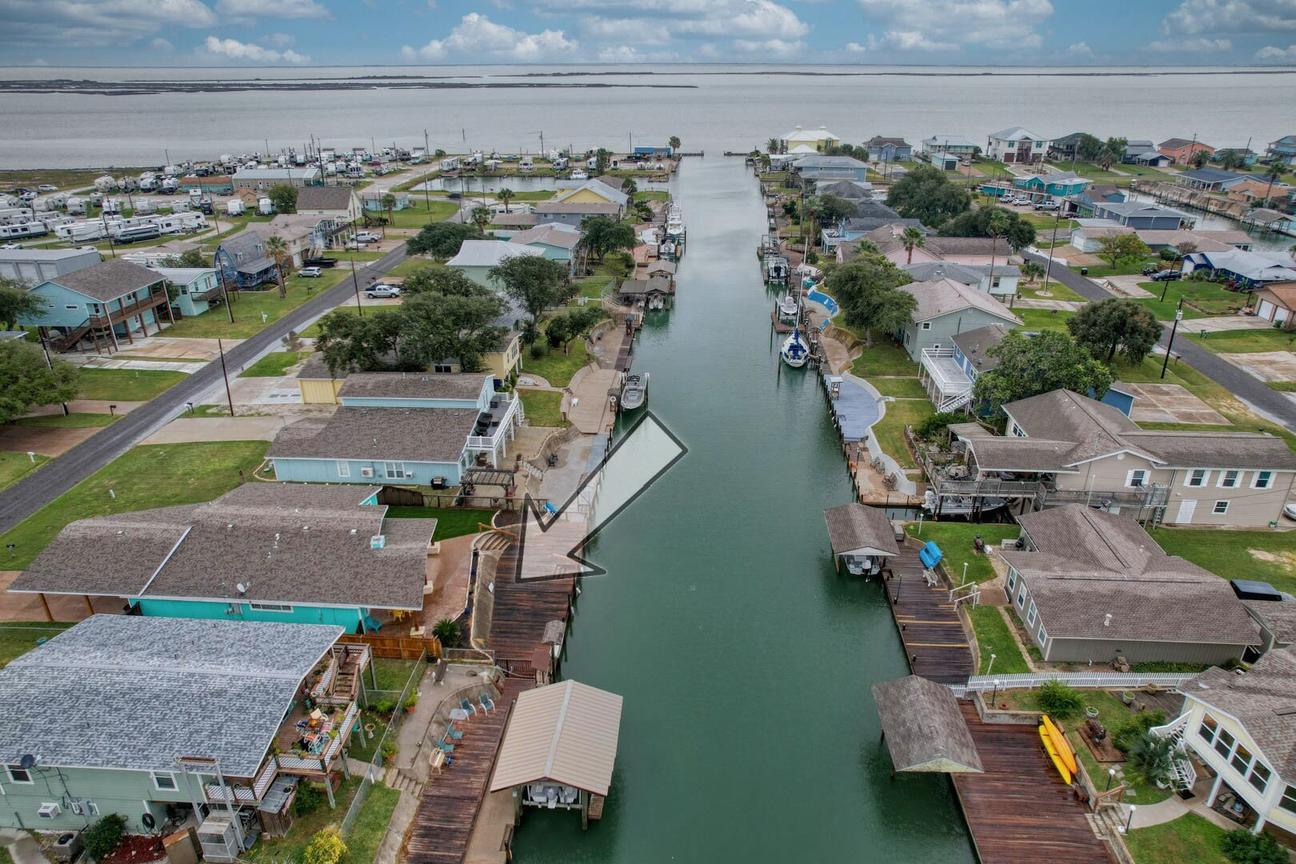 Aerial view of a canal lined with homes and docks, with an arrow pointing to the house and Estes Flats in the distance.