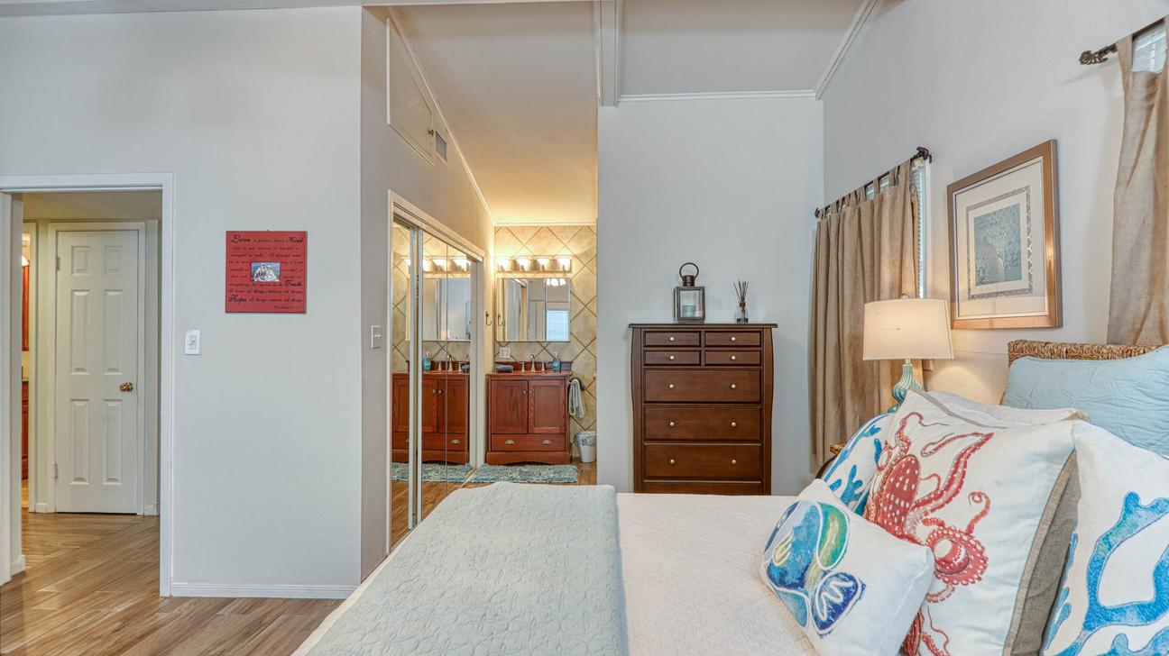 Primary bedroom with king bed, octopus-print pillows, a wooden dresser, and mirrored closet doors leading to a vanity area.