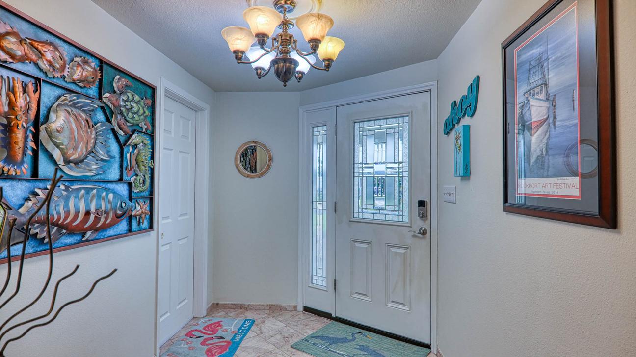 Front entry hall with glass-panel front door, chandelier, framed sailboat print, and large fish wall art.
