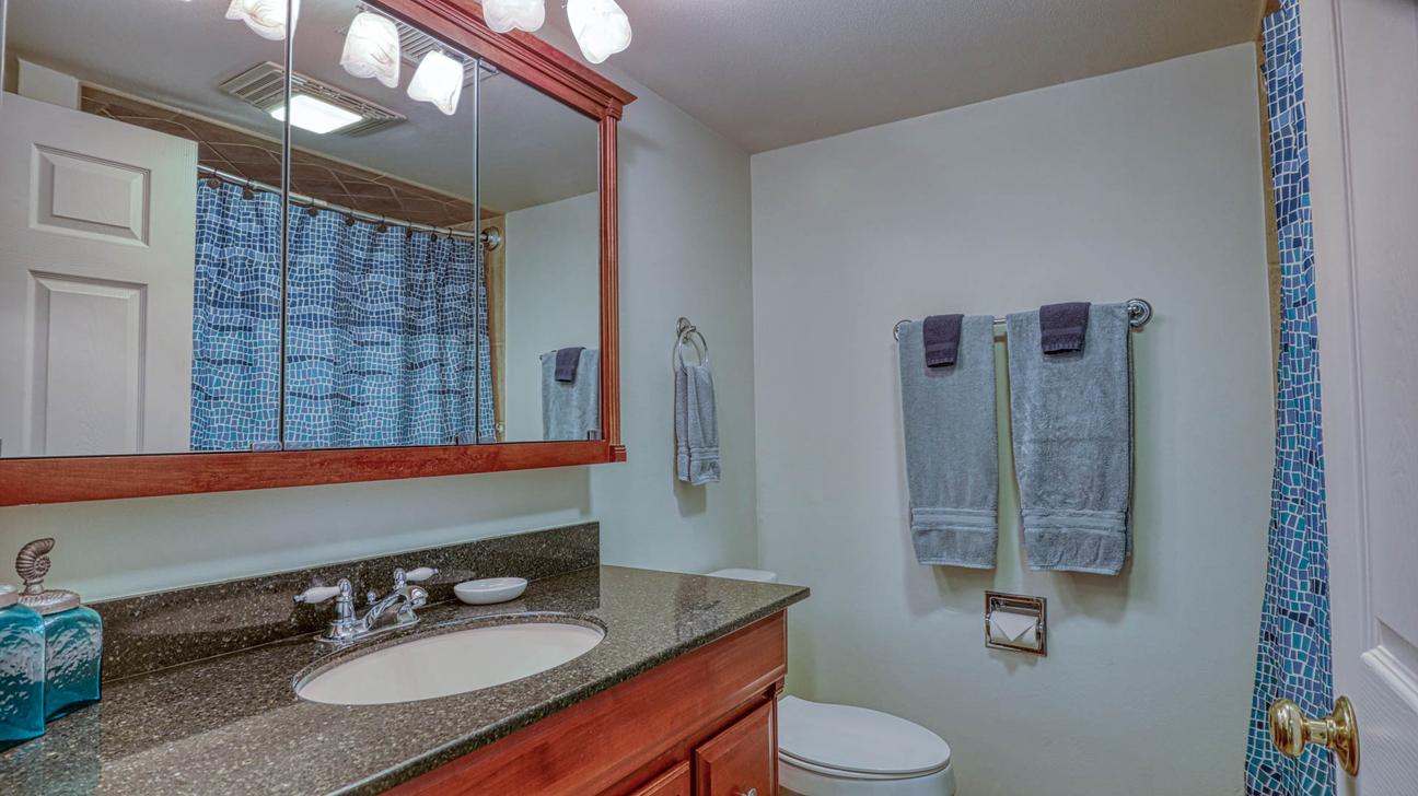 Bathroom with granite vanity, wood-framed mirror, toilet, bath towels, and blue patterned shower curtain.