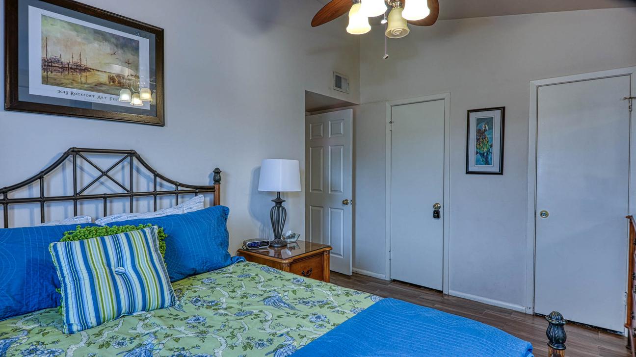 Queen bed with blue and green bedding, a nightstand lamp, ceiling fan, and two closet doors.