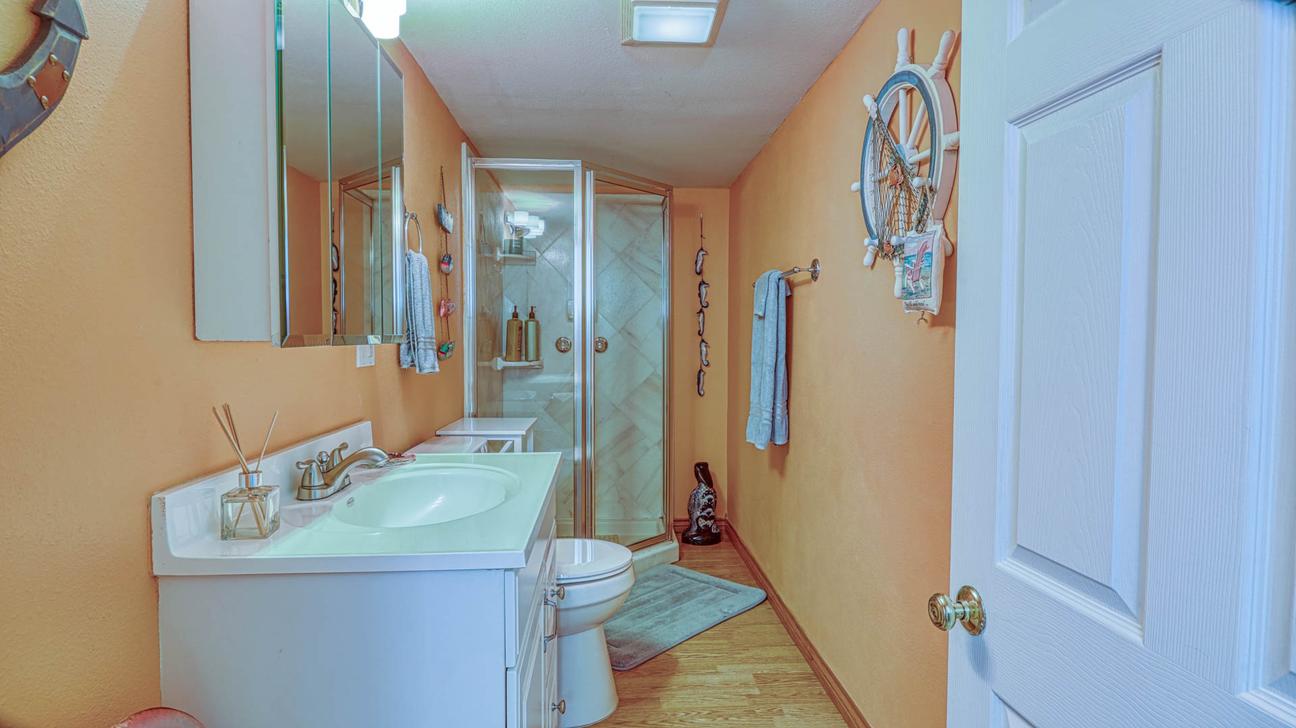 Bathroom with orange walls, white vanity, toilet, and glass-enclosed shower.