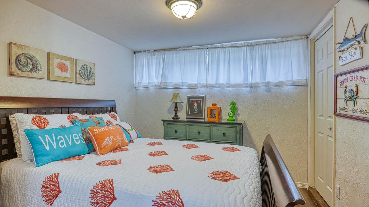 Bedroom with queen sleigh bed, white quilt with coral print, Waves pillow, green dresser, and window with sheer curtains.