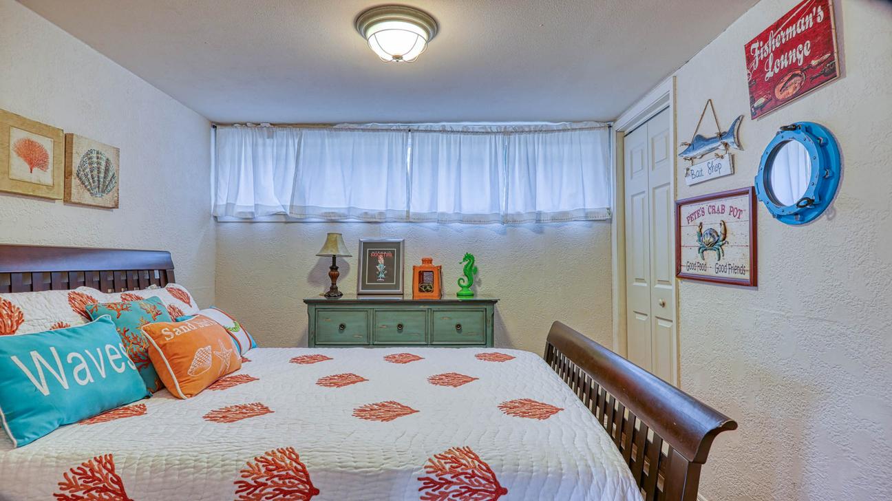 Queen sleigh bed with coral-print quilt, green dresser, porthole mirror, and fish-themed signs on the wall.