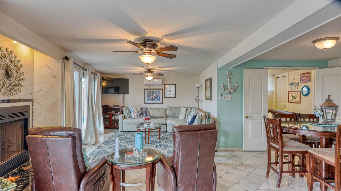 Living room with fireplace, two leather recliners, sectional sofa, wall-mounted TV, and a dining table at right.