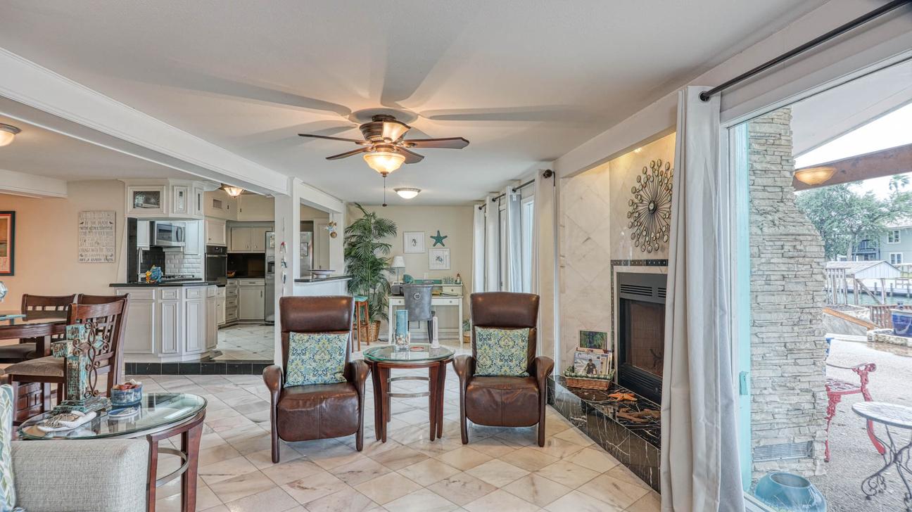 Living room seating with two leather chairs, a stone-accented fireplace, and glass doors opening to the patio.