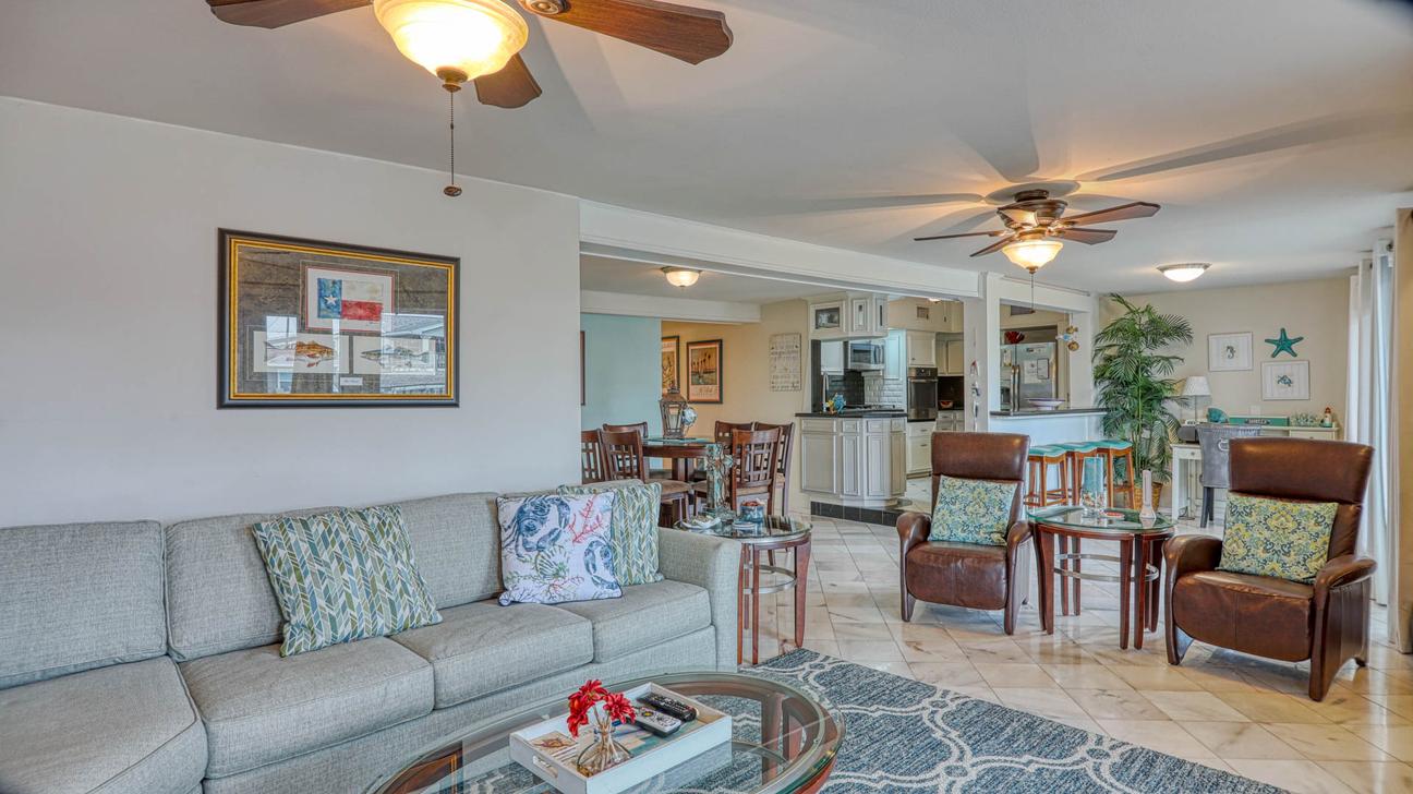 Living room with gray sofa, two leather chairs, round side tables, and a view through to the dining area and kitchen.