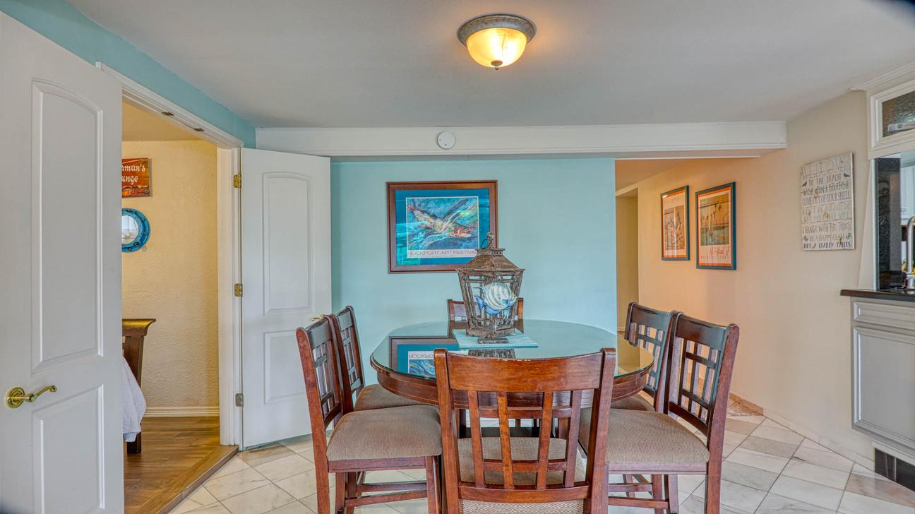 Round dining table with six wooden chairs, a teal accent wall with framed fish art, and doorways to adjacent rooms.