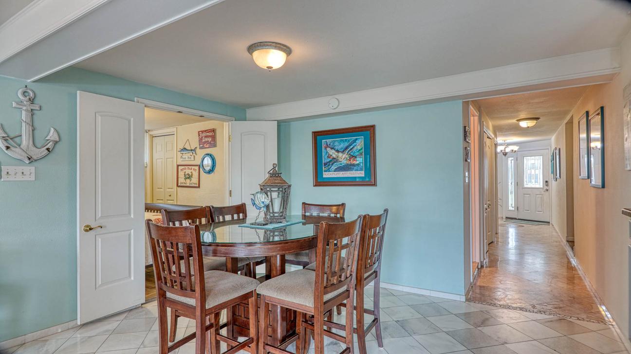 Round dining table with chairs beside a teal accent wall, with a tiled hallway leading toward the front entry.