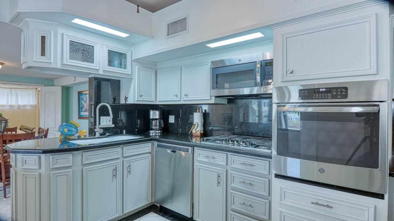 Kitchen with white cabinets, black countertops, stainless steel wall oven, microwave, dishwasher, and gas cooktop.