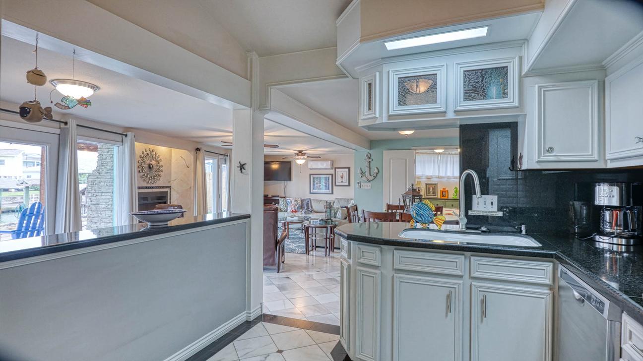 Kitchen sink and white cabinets with a dark countertop, looking through to the living room and glass doors.