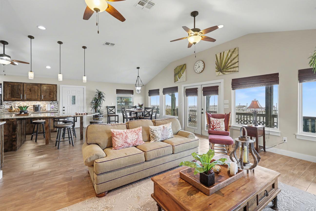 Living room with beige sofa, rocking chair, and wood coffee table; French doors and windows show a deck railing and piers beyond.