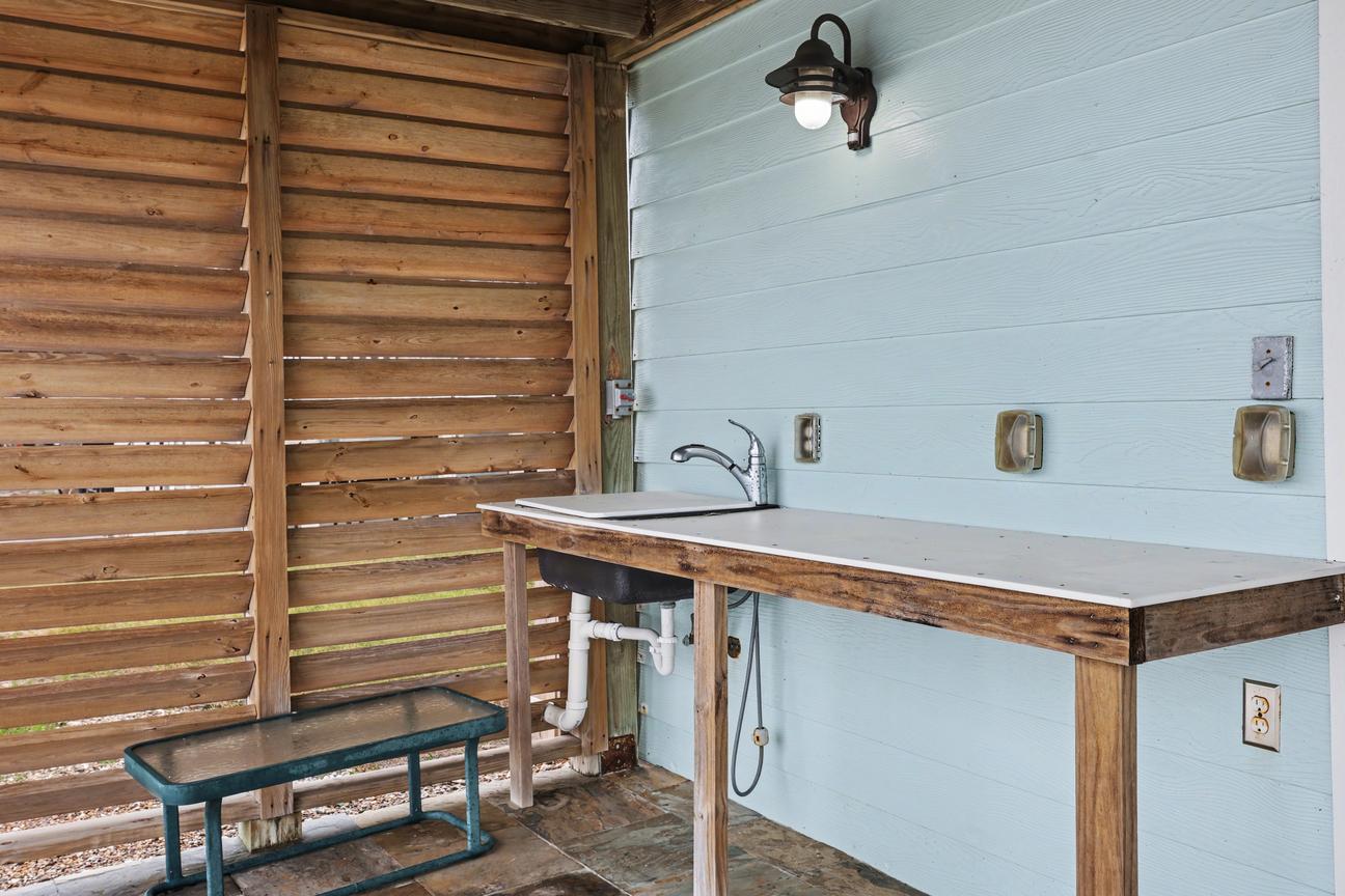 Covered outdoor fish cleaning station with a white countertop and sink with pull-down faucet, wall light, and wooden louvered privacy screen.