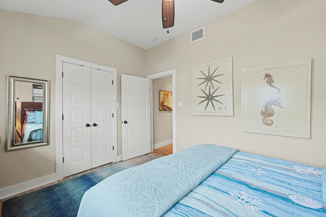 Bedroom corner with a white double-door closet, open door to the hallway, wall mirror, seahorse and starfish prints, and turquoise bedding.