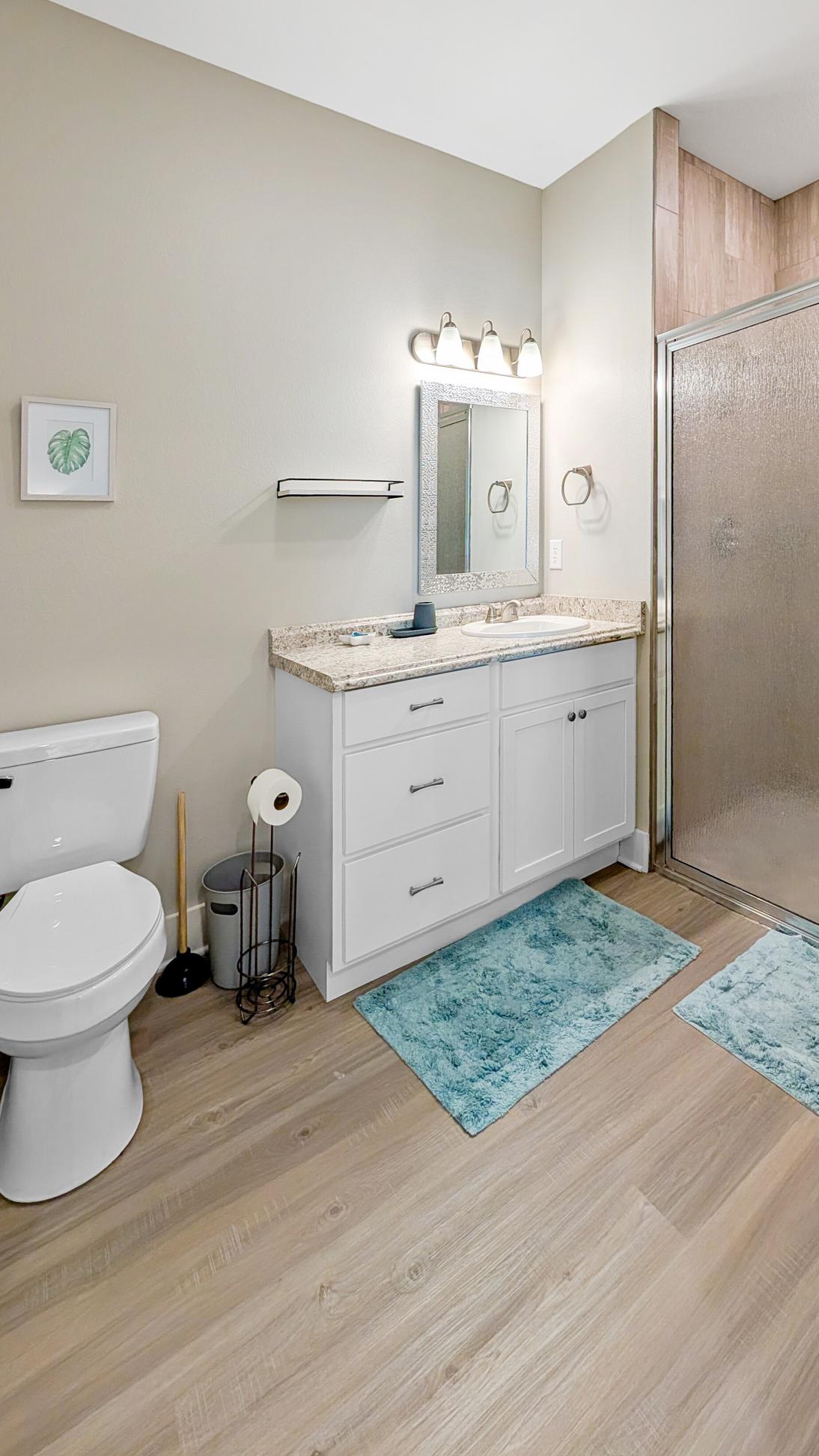 Large bathroom with tiled walk in shower, vanity, sink, toilet. 