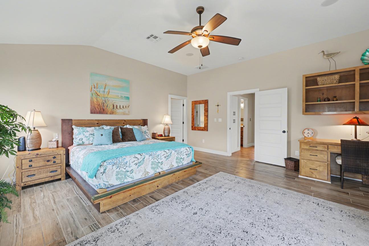 Primary bedroom with king bed and nightstands, a wood desk with chair and lamp, open wall shelves, and two open doorways.