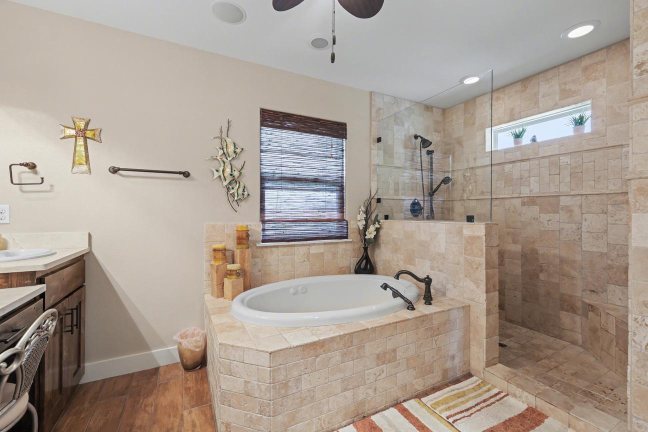 Bathroom with tiled drop-in tub and an open walk-in shower with glass panel, handheld showerhead, and high window with plants.