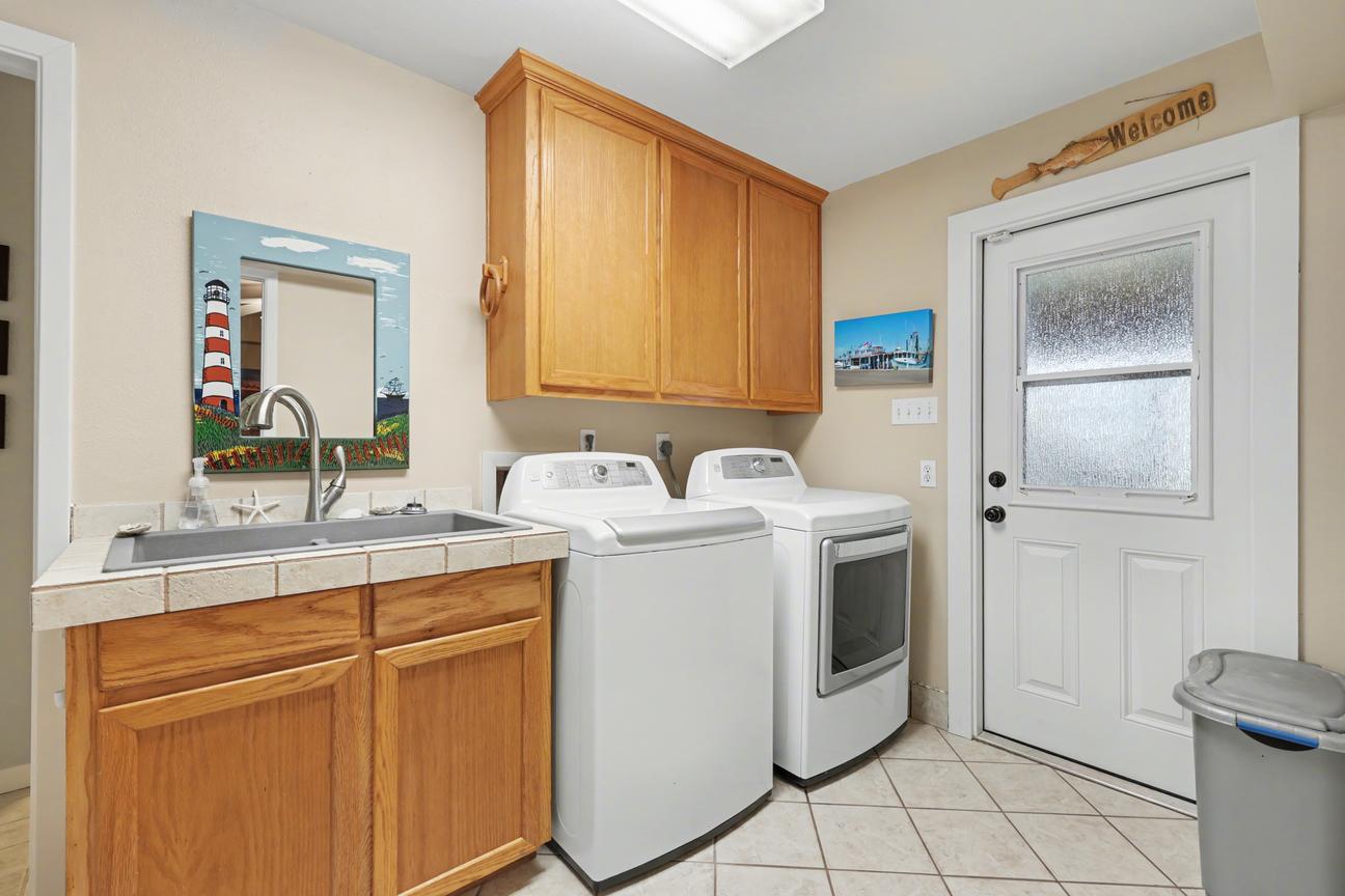 Laundry room with top-load washer, dryer, utility sink with wood cabinet, upper cabinets, and a half-glass exterior door.