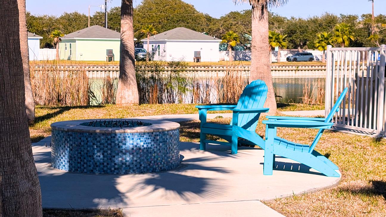 Large, round firepit surrounded by  chairs and palm trees. 