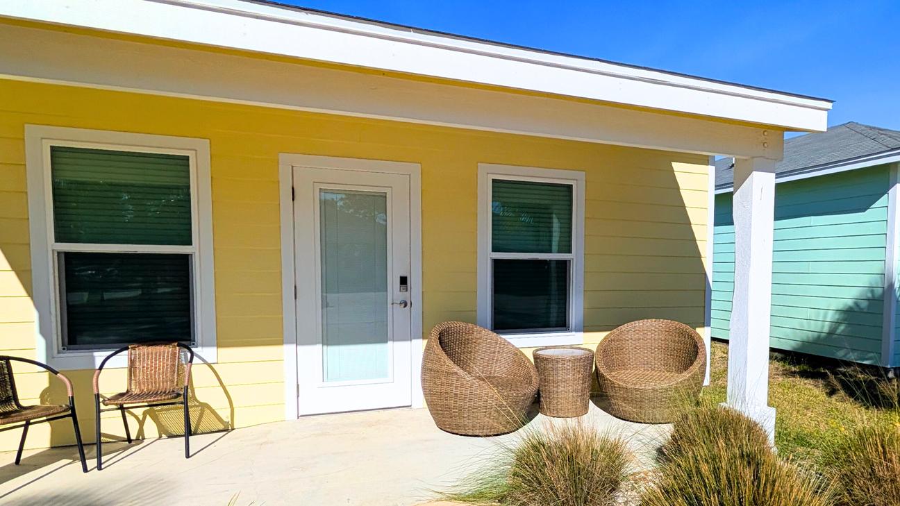 Single story yellow home with tan patio furniture and plenty of parking. 