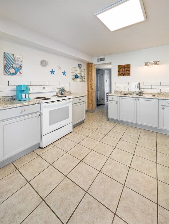 Spacious kitchen with white cabinets, white stove, granite countertops, tile flooring, and coastal wall decor accents.