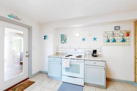 Kitchen area with white stove, light blue and white cabinets, granite countertops, coastal wall decor, and a glass door leading outside.