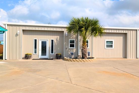 Modern single-story coastal home in Rockport, Texas with light siding, large driveway, palm tree landscaping, and double garage doors.