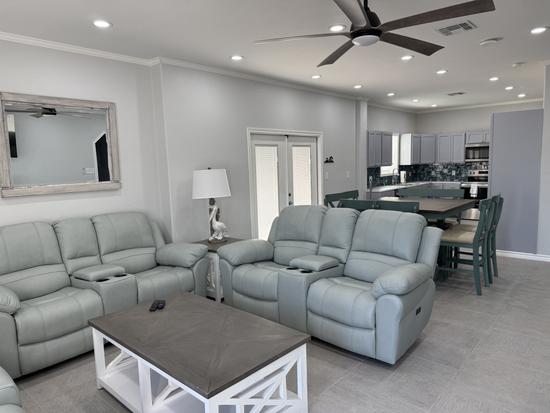 Bright coastal-style living room with plush reclining sofas and chairs, soft neutral décor, modern coffee table, and open seating arrangement in a comfortable vacation rental.