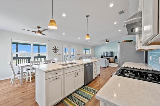 Open coastal kitchen with a large island, white cabinetry, modern appliances, and an adjoining dining and living area.