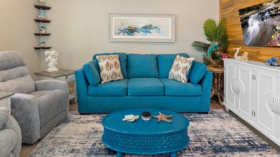Living room with a blue sofa, recliner, round coffee table with coastal decor, wall art of crabs, and a TV on a cabinet with wood accent wall.