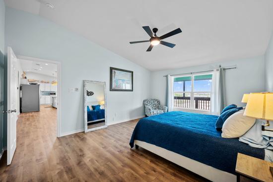 Coastal primary bedroom with a king bed, blue bedding, wood-look floors, an accent chair, and large windows.