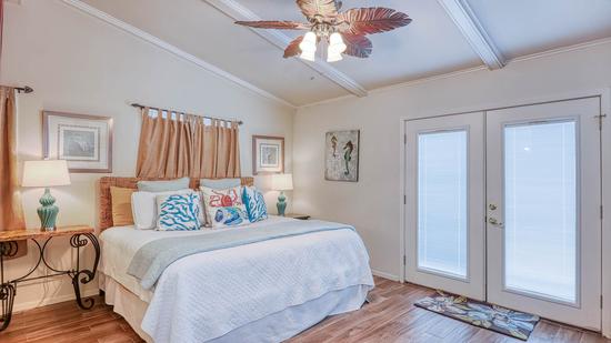 Primary bedroom with king bed, coastal-print pillows, two teal lamps, a ceiling fan, and white French doors.