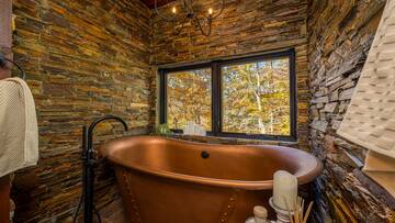 Clawfoot style tub surrounded in faux rock wall.